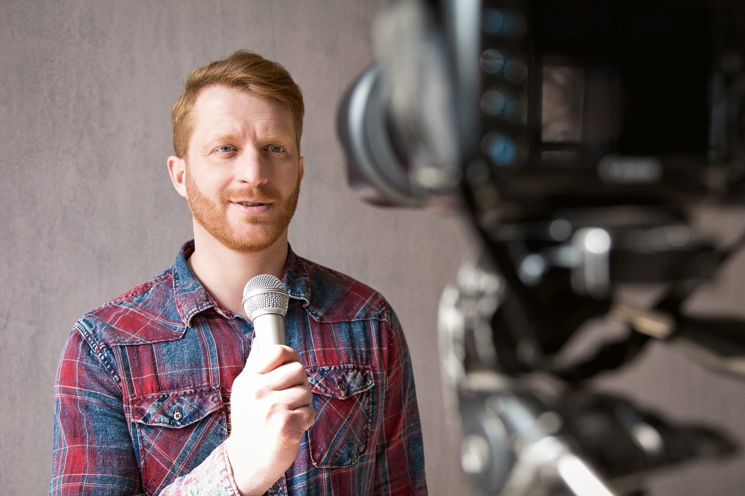 man videoing himself holding microphone his hand stunning young man with red hair wearing shirt standing front video camera speaking into microphone
